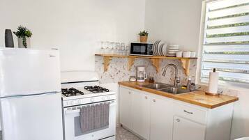 A compact kitchen with a refrigerator, stove, oven, microwave, and a wooden countertop.