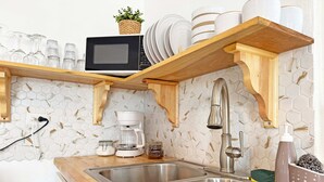 A kitchen with a stainless steel sink, wooden shelves, a microwave, and a hexagonal tile backsplash. - Beach House with Pool in Playa Santa - Casa Perla (Guánica)