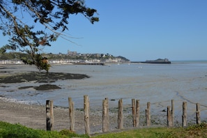 A coastal landscape with a wooden fence, a clear sky, and a distant view of buildings and a rocky outcrop.
