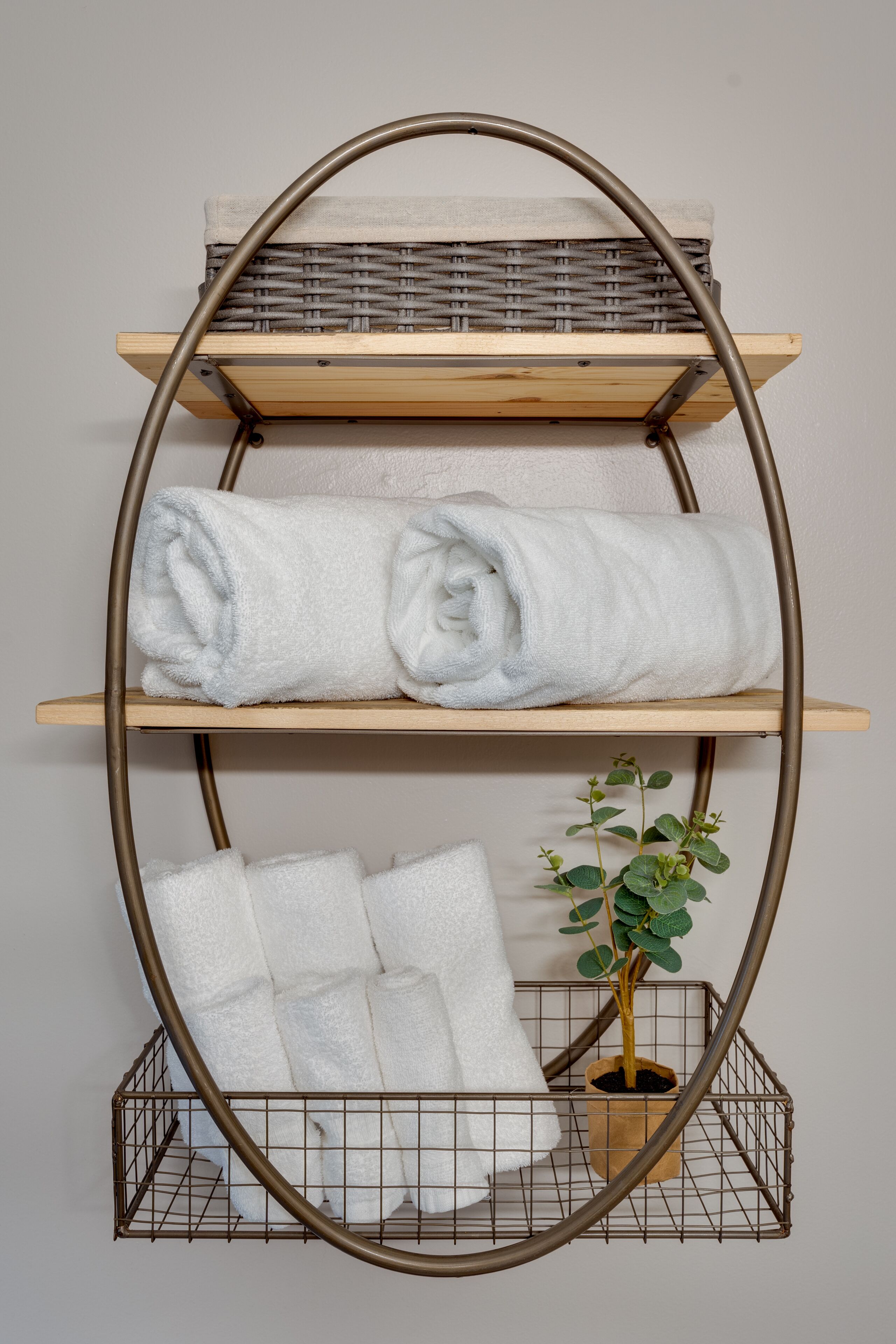 A metal-framed shelf with three tiers, each holding rolled towels and a potted plant.