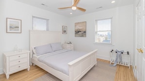 Un dormitorio con cama, mesitas de noche, un velador, ventilador de techo y ventanas con persianas.