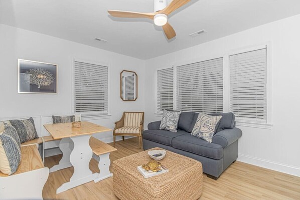 A modern living room with a grey sofa, a wooden dining table, and a ceiling fan.