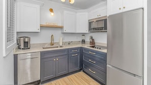 Una cocina moderna con armarios blancos, un refrigerador de acero inoxidable, una cafetera y un microondas integrado.