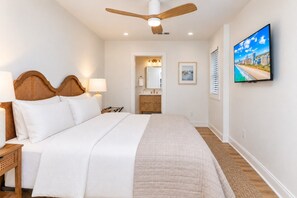 A hotel room with a bed, a ceiling fan, a television, and a bathroom visible through an open door.