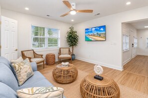 A spacious living room with a blue sofa, two striped chairs, a large potted plant, and a painting of a beach scene.