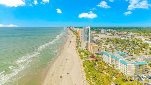 Un paysage urbain côtier avec une plage, des immeubles de grande hauteur et un ciel dégagé.