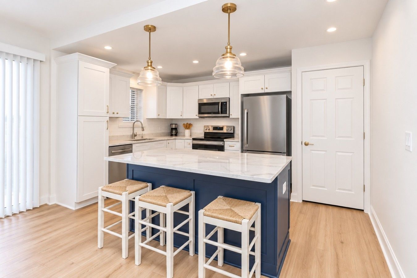 A modern kitchen with white cabinets, a central island with bar stools, stainless steel appliances, and pendant lighting.