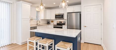 A modern kitchen with white cabinets, a central island with bar stools, stainless steel appliances, and pendant lighting.
