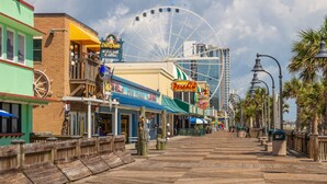 A boardwalk with shops, a Ferris wheel, and a modern building in the background.