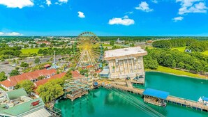 A waterfront amusement park with a Ferris wheel, a water tower, and a building with columns.