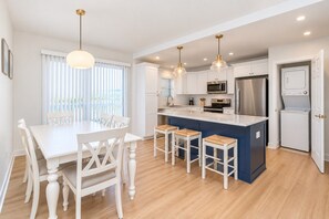 A modern kitchen with white cabinetry, a central island with bar stools, and stainless steel appliances. - Perfect Myrtle Beach Cottage (Myrtle Beach)