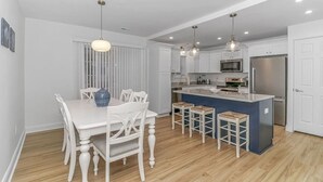 Une cuisine moderne avec des meubles blancs, un îlot central doté de tabourets et un coin repas avec une table et des chaises blanches.