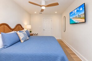 Ein Schlafzimmer mit einem Bett, einem Deckenventilator, einem Fernseher und einer Tür.