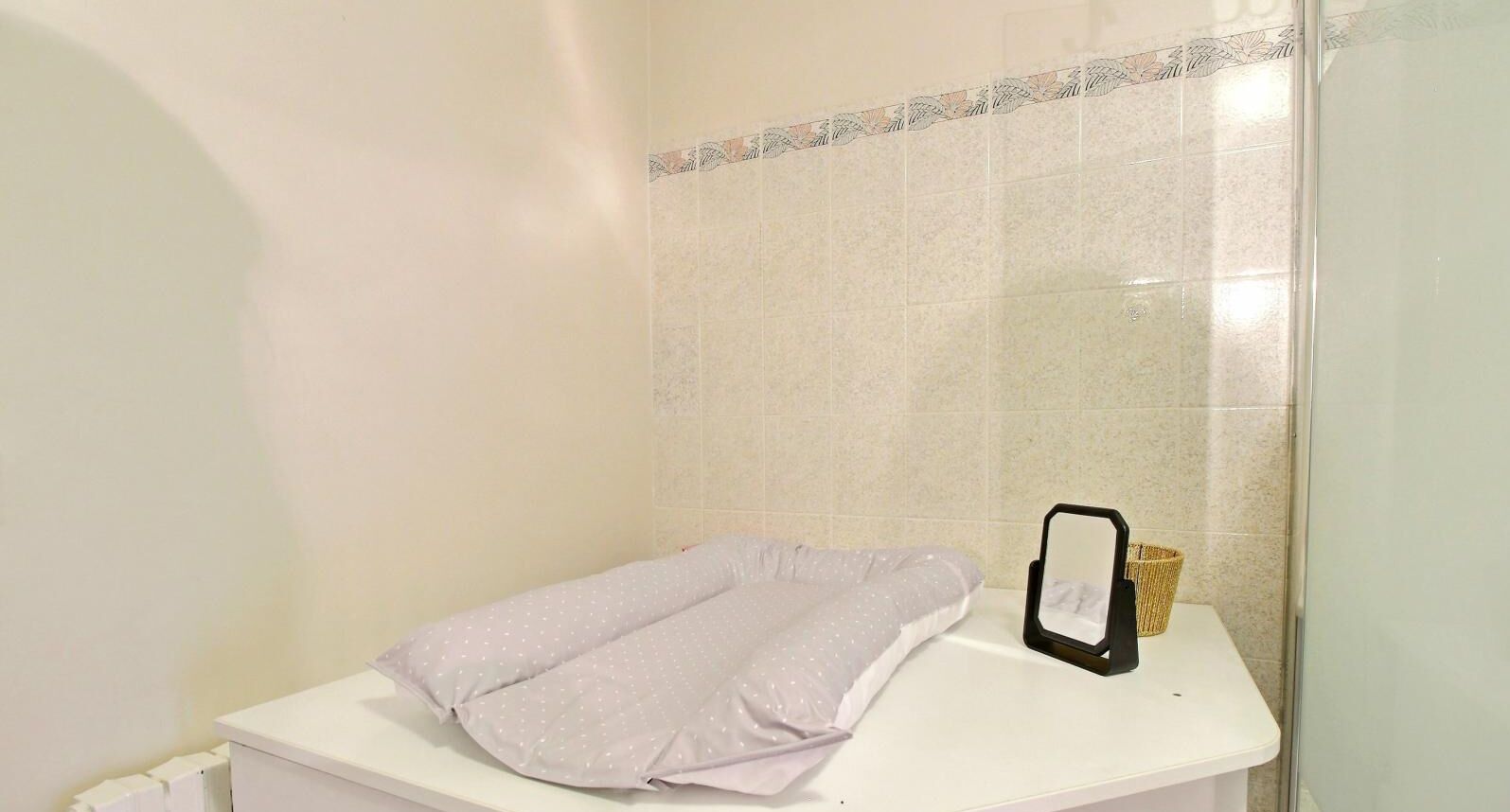 Une salle de bain avec un comptoir blanc, une serviette, un miroir et un panier en osier.