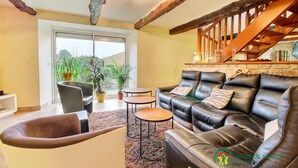 Amplia sala de estar con un sofá de cuero, una mesa de centro y un sillón. Se observa una escalera con barandillas de madera que conduce a un nivel superior.