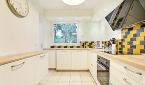 Une cuisine moderne avec des armoires blanches, un plan de travail en bois, une fenêtre donnant sur les arbres et un pare-feu en carreaux.