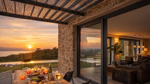 Comedor con mesa lista para una comida, con vista a un paisaje escénico del atardecer sobre el agua.