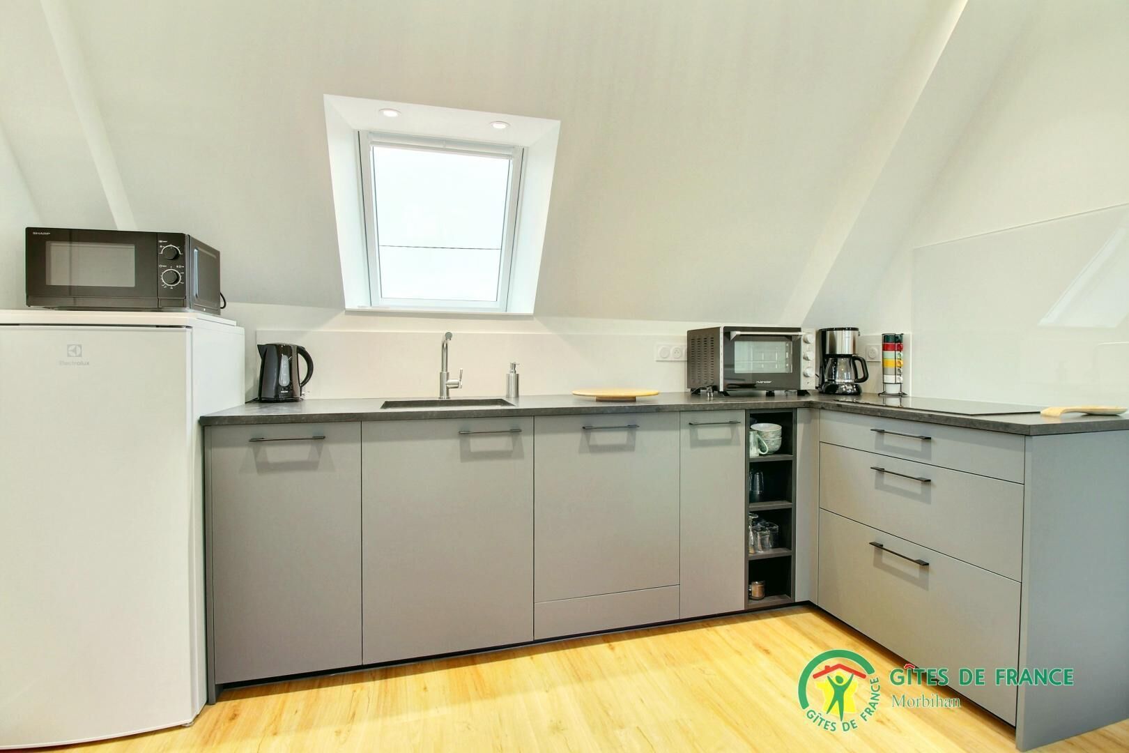 A modern kitchen with grey cabinets, a microwave, a coffee maker, and a small window above the sink.