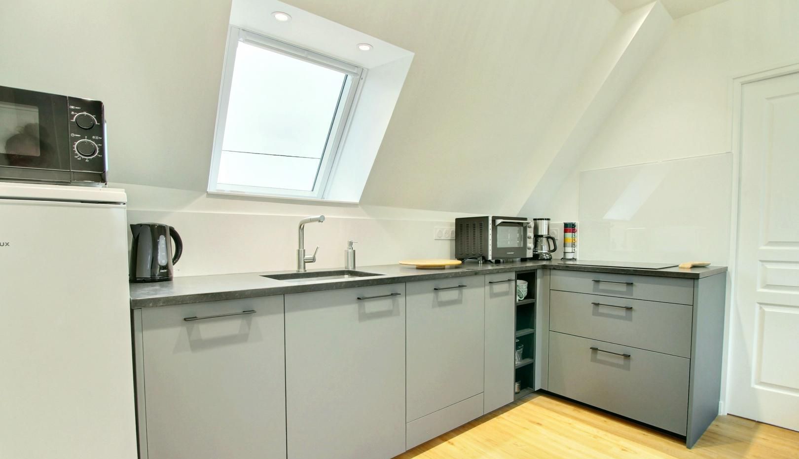 A modern kitchen with grey cabinets, a built-in microwave, a coffee maker, and a window above the sink.