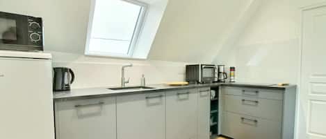 A modern kitchen with grey cabinets, a built-in microwave, a coffee maker, and a window above the sink.