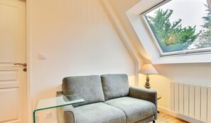 A small, modern living room with a grey sofa, a glass coffee table, and a window with a view of trees. - Ker Zen - Locmariaquer (LOCMARIAQUER)