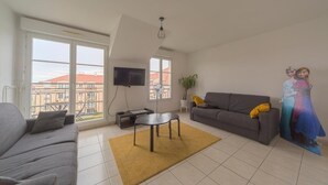 Una sala de estar con un sofá, una mesa de centro, un televisor y un ventanal grande.