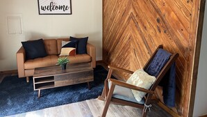A living room with a brown leather sofa, a wooden coffee table, a blue shaggy rug, and a wooden rocking chair with a cushion. - The Loft  Private Cabin Near Hulaween & Spirit of the Suwannee (Live Oak)