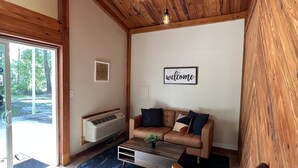 A cozy living room with a wooden ceiling, a sofa, a coffee table, and a swing chair. - The Loft  Private Cabin Near Hulaween & Spirit of the Suwannee (Live Oak)