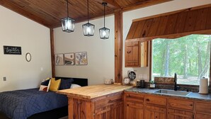 A cozy bedroom with a large bed, a wooden desk, and a window with a view of trees. - The Loft  Private Cabin Near Hulaween & Spirit of the Suwannee (Live Oak)
