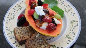 Ein Teller mit einem Obstsalat, darunter Trauben, Himbeeren, Brombeeren und ein Melonenscheibchen, dazu zwei Brotscheiben.