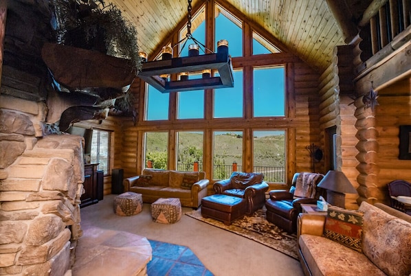 Interior de una cabaña de troncos con chimenea de piedra, ventanas amplias y mobiliario de cuero.