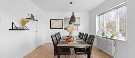 Comedor con una mesa de madera, sillas negras, una lámpara colgante y una ventana con vistas a árboles.