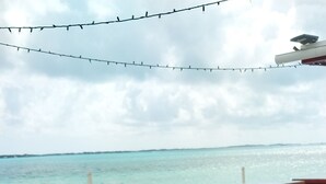 A beachside patio with wooden tables and chairs, a concrete floor, and a view of the turquoise sea. - 
5 mins away from public beach and 3 min from grocery store! (The Forest)