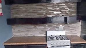 A kitchen with dark wooden cabinets, a stainless steel gas stove, and a tiled backsplash. - 
5 mins away from public beach and 3 min from grocery store! (The Forest)