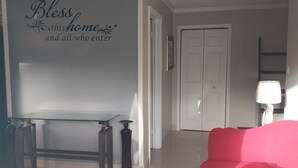 A living room with a glass-top table, two chairs, a red sofa, and a wall with a decorative sign. - 
5 mins away from public beach and 3 min from grocery store! (The Forest)