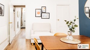 A modern living room with a white sofa, a wooden dining table with a vase of greenery, and framed artwork on the wall. - Alices Central Stay Parking  Motor Point Arena (Sneinton)