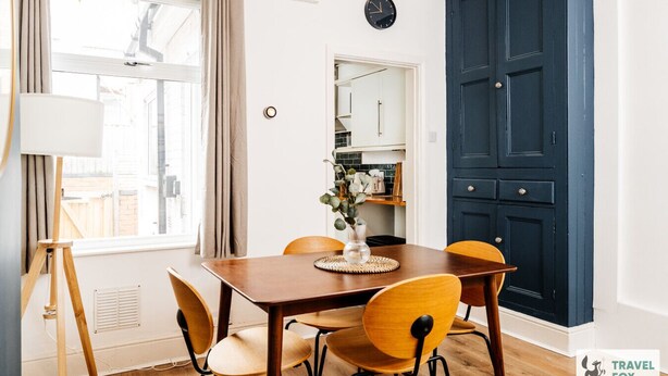 A dining area with a wooden table, four chairs, a vase with flowers, and a clock on the wall. - Alices Central Stay Parking  Motor Point Arena (Sneinton)