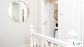 A staircase with a white balustrade leading to a bathroom with a marble wall and a round mirror with a gold frame. - Alices Central Stay Parking  Motor Point Arena (Sneinton)