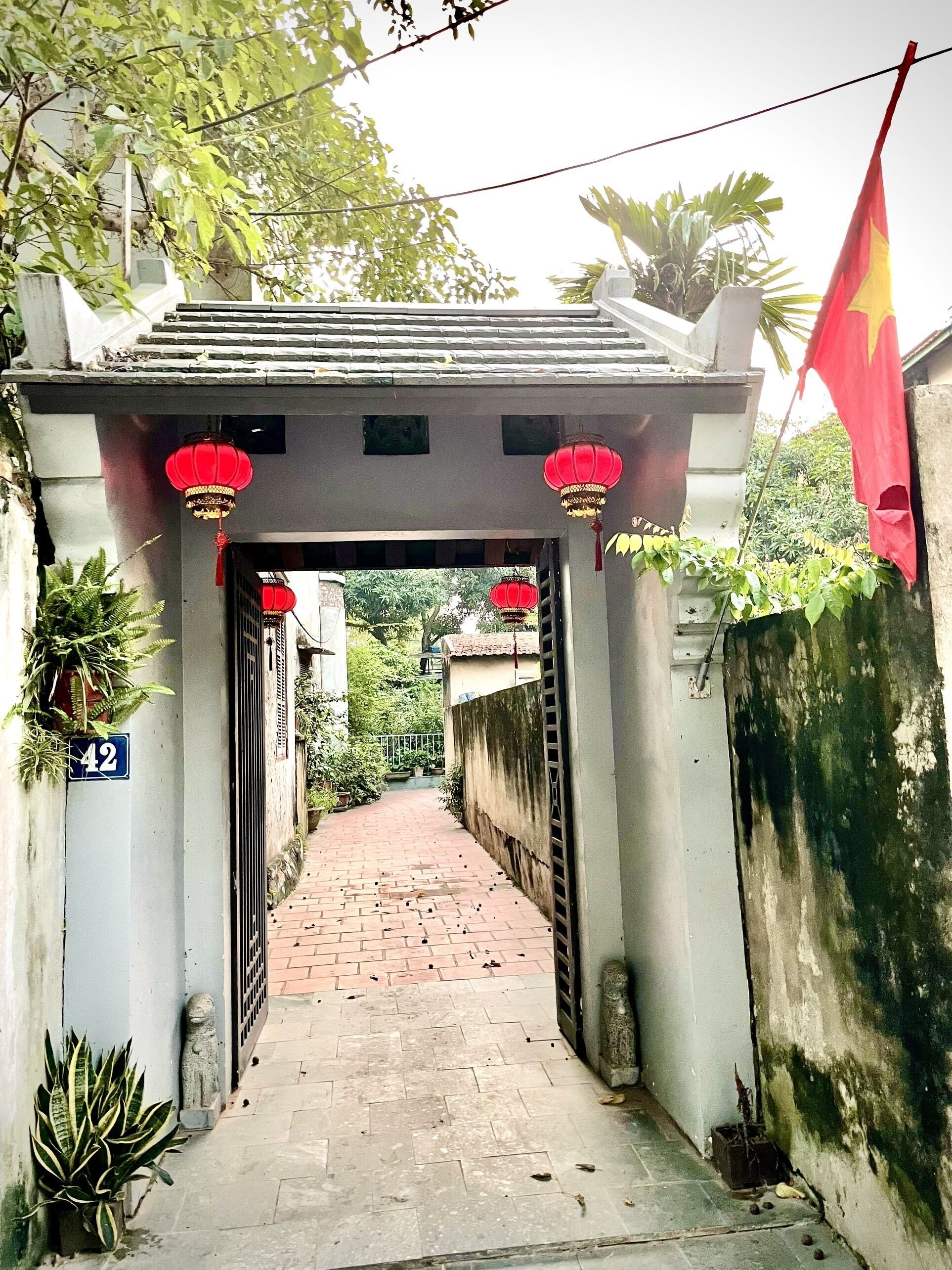 A pathway leading to a building entrance with a traditional archway, red lanterns, and a flag.