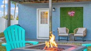 Un patio con un hogar, dos sillas de mimbre y un letrero de neón en la pared.
