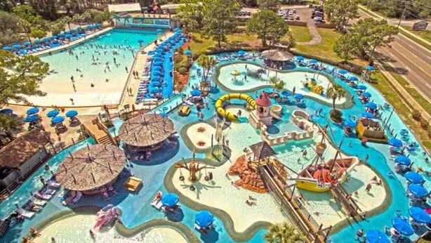 Vista aérea de un parque acuático con múltiples piscinas, toboganes y zonas de sol.