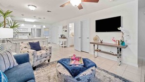 Una sala de estar amplia con un ventilador de techo, un televisor de pantalla plana y una zona de comedor con mesa y sillas de madera.