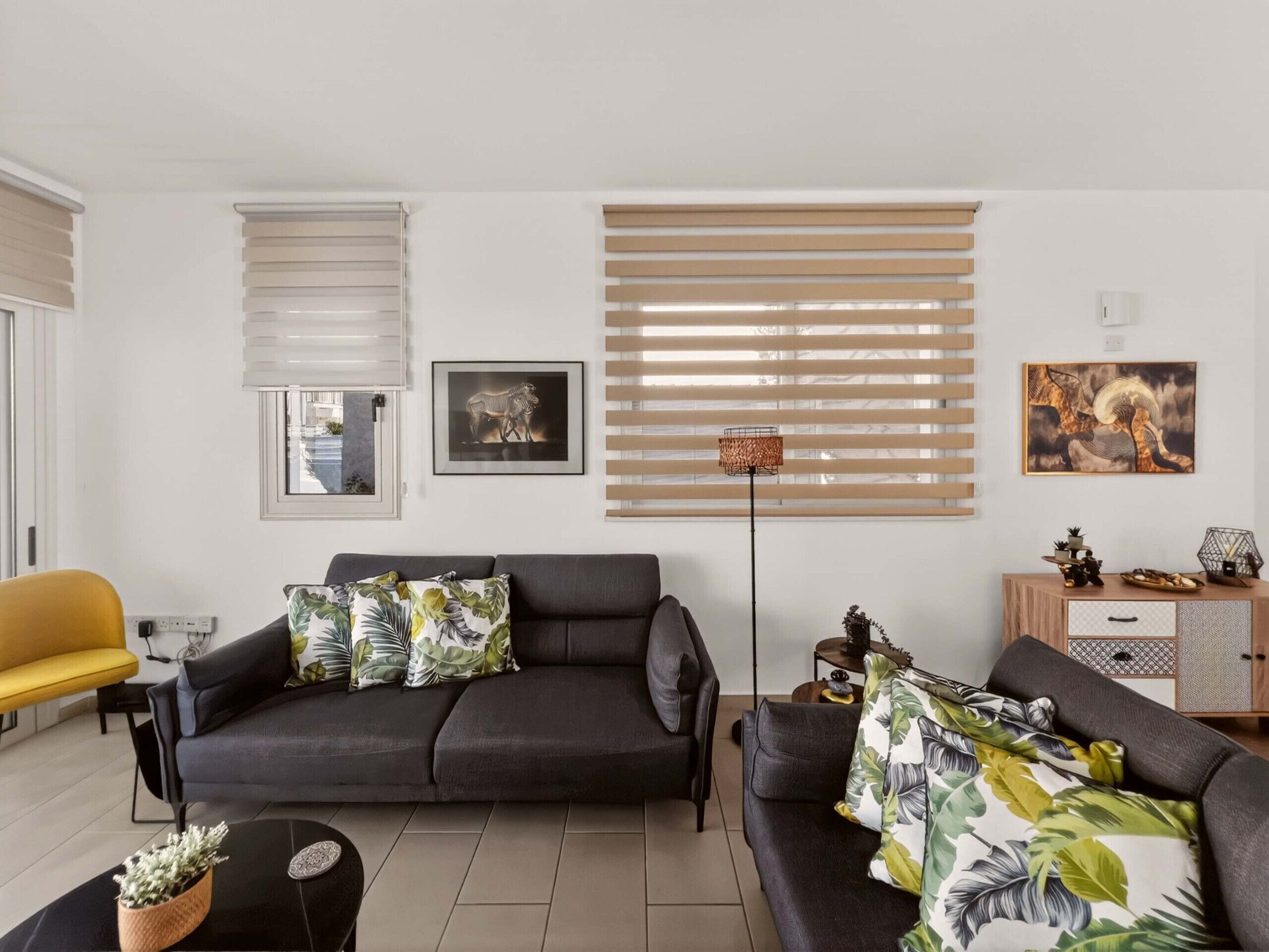 A living room with a sofa, a yellow chair, a floor lamp, and a cabinet with decorative items.
