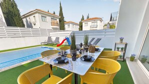A poolside dining area with a table set for four, surrounded by yellow chairs, and a slide in the background. - Villa Allegra: Private Pool & Modern Comfort (Protaras)