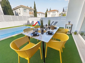 A poolside dining area with a table set for four, surrounded by yellow chairs, and a slide in the background.