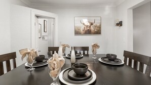 Une salle à manger avec une table en bois foncé dressée pour quatre personnes, des murs blancs, un tableau encadré représentant un yak et une lucarne au plafond.