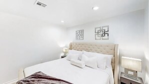 Une chambre à coucher avec un grand lit, une tête de lit, des tables de chevet et des œuvres d’art murales.
