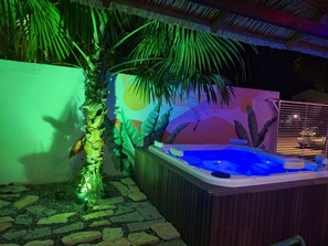 Un bain à remous doté d’une terrasse en bois et d’un chemin de pierre menant à celui-ci.