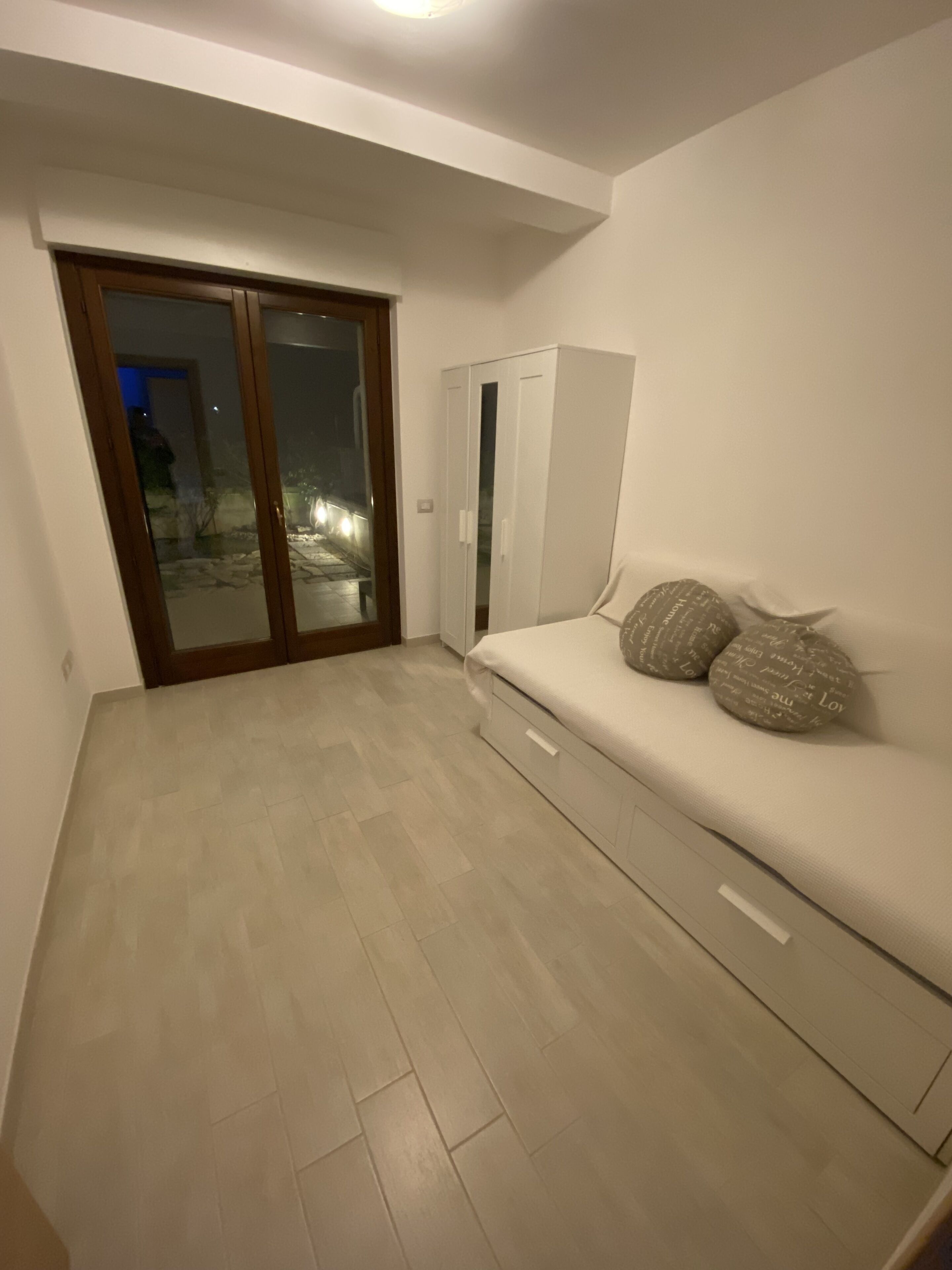 Ein Schlafzimmer mit Schiebetür zum Balkon, einem Bett mit Kissen und einem Kleiderschrank.