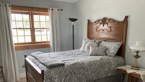 Un dormitorio con cama de madera, ropa de cama con estampado de cebra, lámpara de noche y ventana con cortinas.